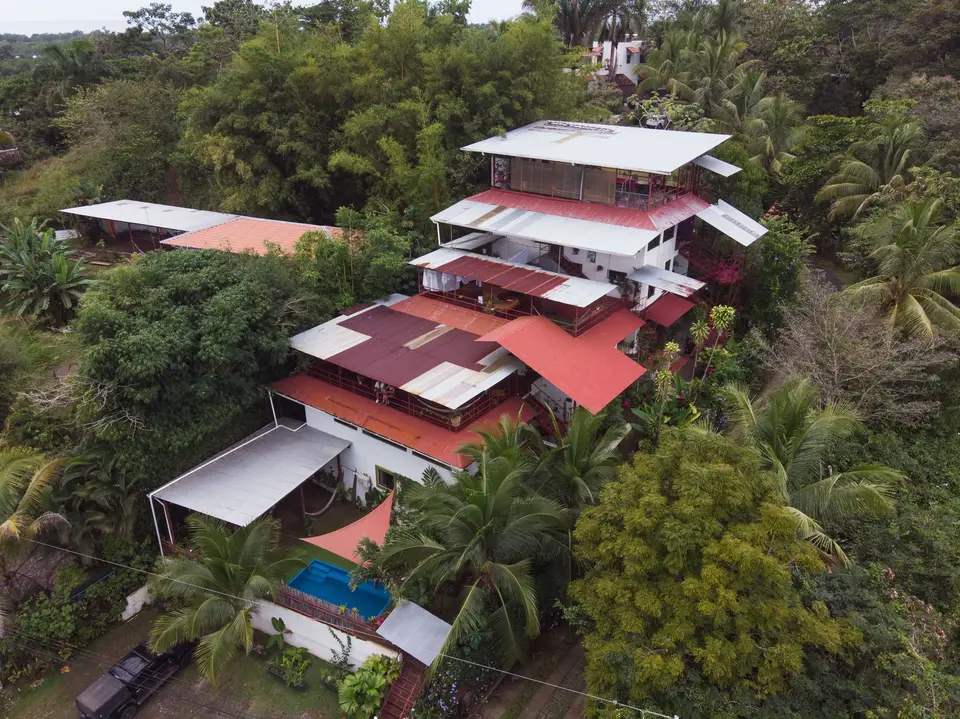 Aerial view of Villas Jacquelina: white walls and red roofs stacked up a jungle hillside, the pool glinting at the foot