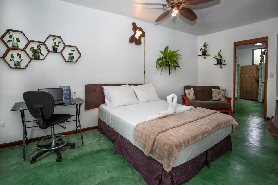Villa Linda: queen bed with a striped throw, desk and chair, plants on hexagon shelves