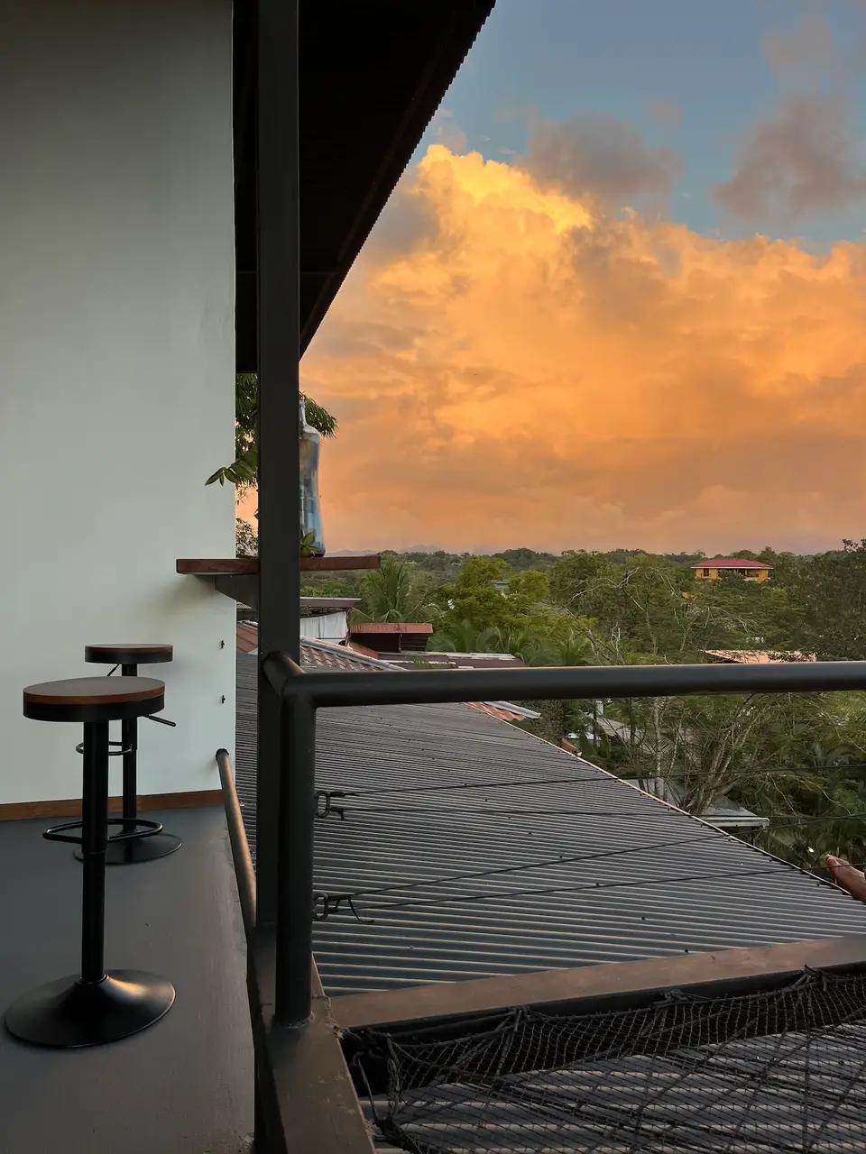 The Bird’s Nest balcony: bar stools and orange sunset clouds over the treetops