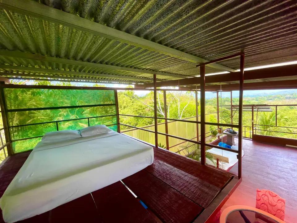 El Palomar: a low double bed on the red floor with the jungle beyond the railing