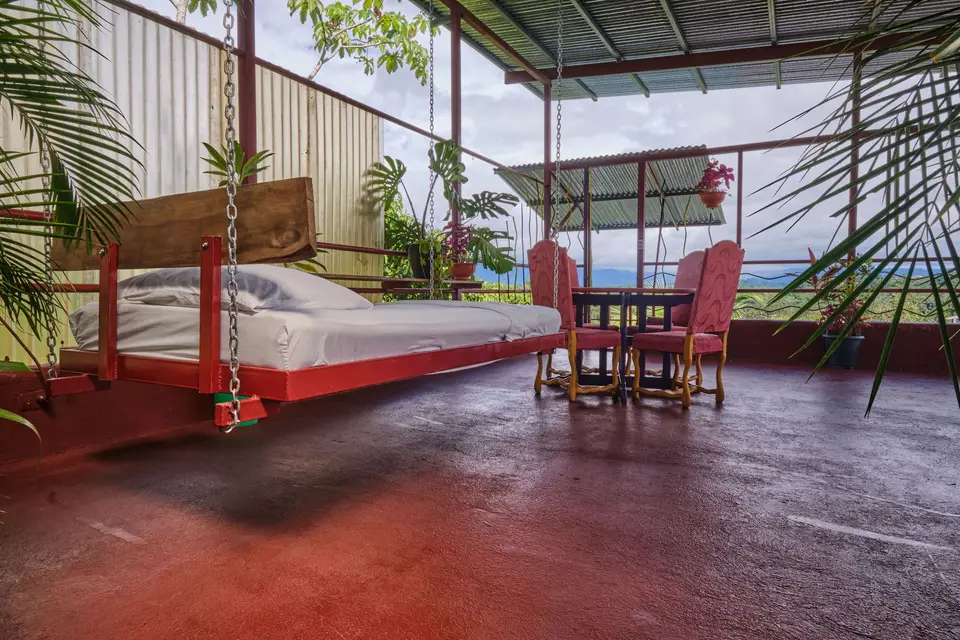 El Palomar: a bed hung on red chains beside a table and red chairs, the valley beyond