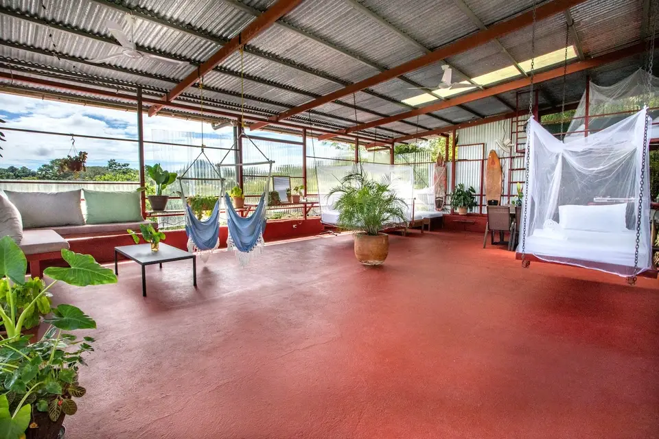 El Palomar: the open-air top floor with a red floor, a bed under a mosquito net and the treetops all around