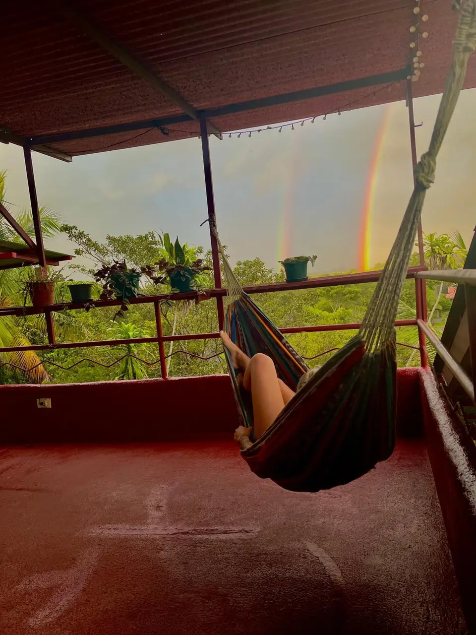 A guest in a hammock on the red terrace, a rainbow over the jungle