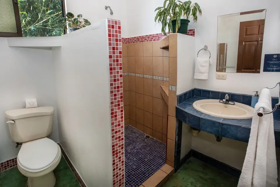 El baño compartido de las habitaciones Villa Sol: ducha enchapada y lavatorio azul