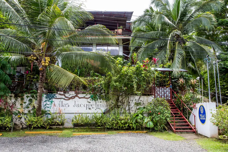 The street front: the Villas Jacquelina sign wall, palms, red stairs and the gravel drive