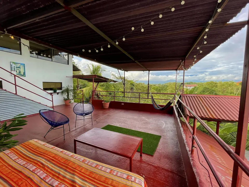 A terrace with string lights, blue egg chairs, a hammock and a day bed over the jungle