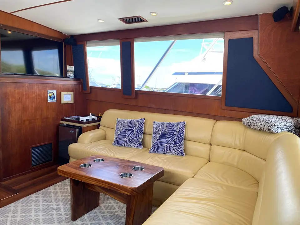 Inside a yacht cabin: a cream leather sofa, a wooden table and wide windows onto the marina.