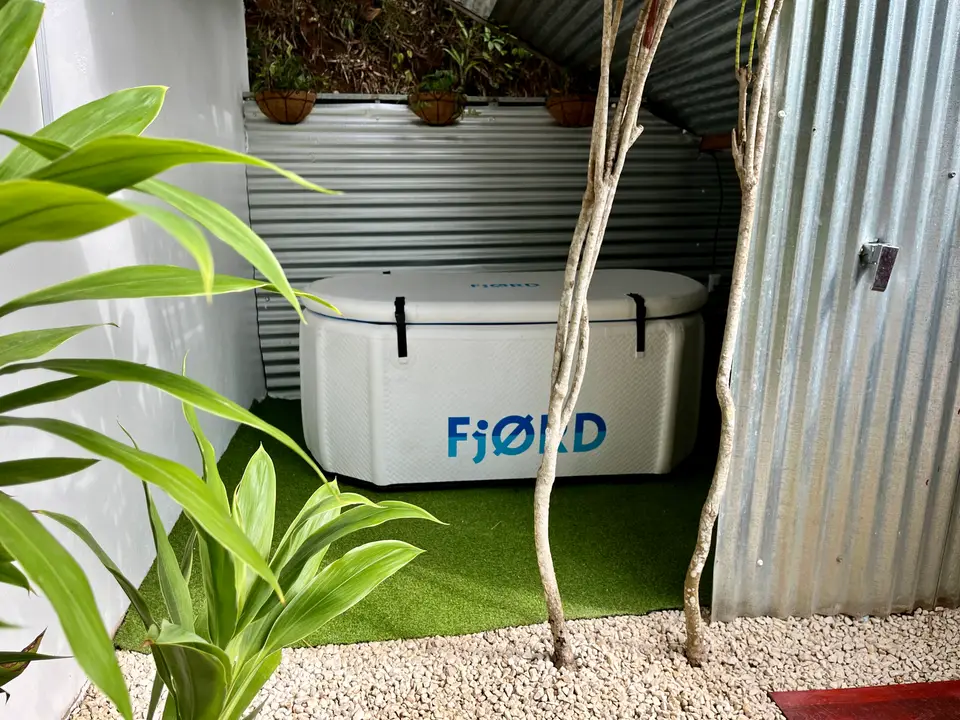 The white two-person cold-plunge tub at Villas Jacquelina, on green turf beside corrugated-metal walls and potted plants.