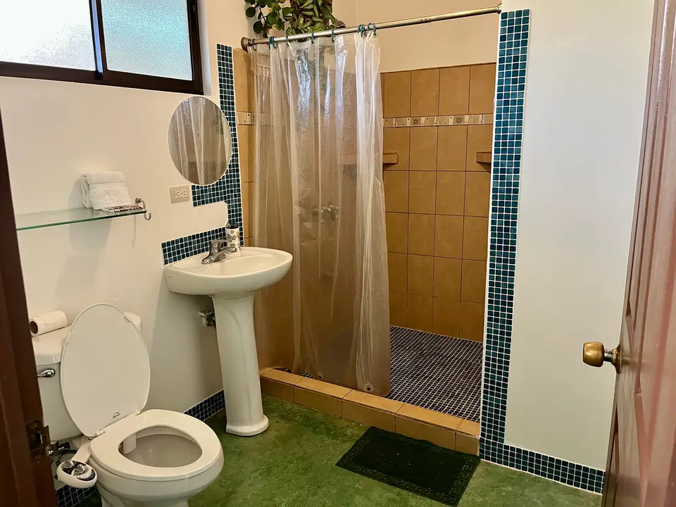 Villa Vista bathroom: pedestal sink, round mirror and a shower trimmed in blue mosaic