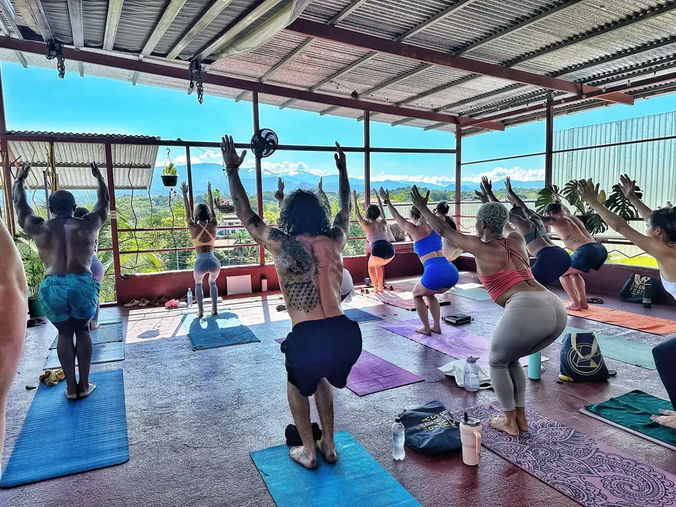 A group yoga class on the rooftop, arms raised, with clouds and mountains beyond